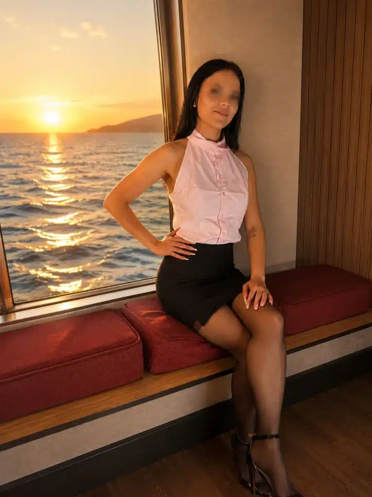Alina in einer ärmellosen rosa Bluse und einem schwarzen Rock sitzt auf einer roten gepolsterten Bank am Fenster.