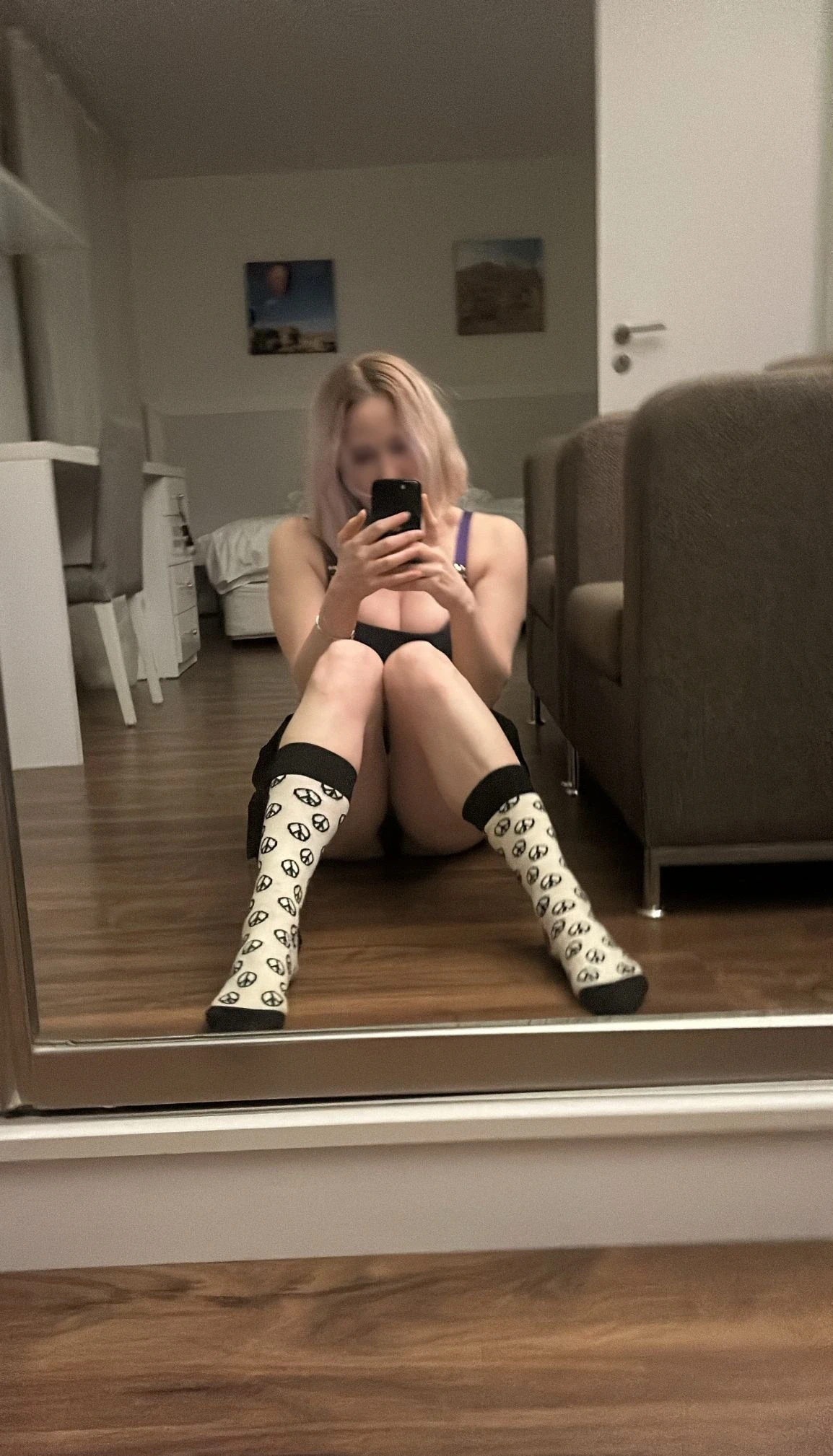 Anna mit schulterlangem Haar sitzt auf dem Boden und macht ein Spiegel-Selfie.
