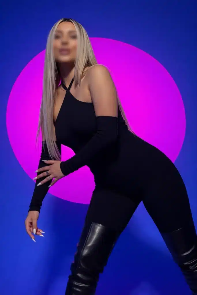 Barbie mit langem blondem Haar posiert vor einem violett-rosa kreisförmigen Licht.