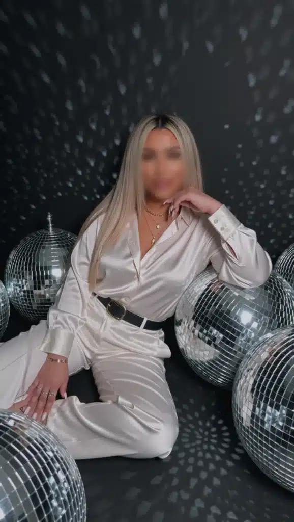 Barbie mit langen blonden Haaren in einem seidig-weißen Outfit posiert zwischen mehreren großen Discokugeln.