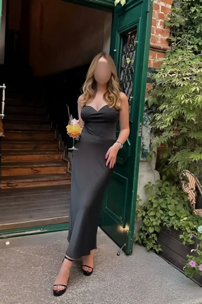 Nikki in einem schwarzen Kleid und hochhackigen Schuhen steht vor einer grünen Tür