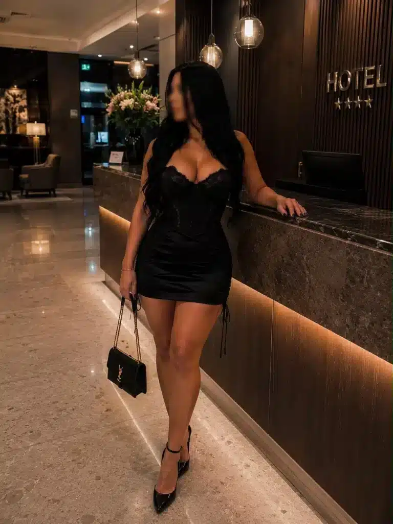 Lexi in einem schwarzen Kleid steht an der Rezeption eines Hotels.