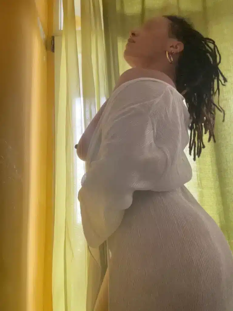 Lolaa poses in front of a green curtain wearing a white, see-through dressing gown