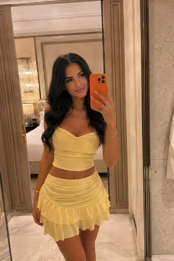 Luna, wearing a stylish yellow two-piece outfit, takes a selfie in the mirror.