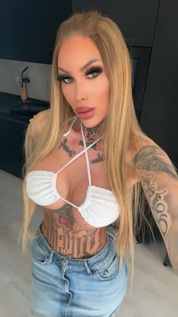 Vanessa, wearing bold makeup and tattoos, poses in a kitchen for a selfie